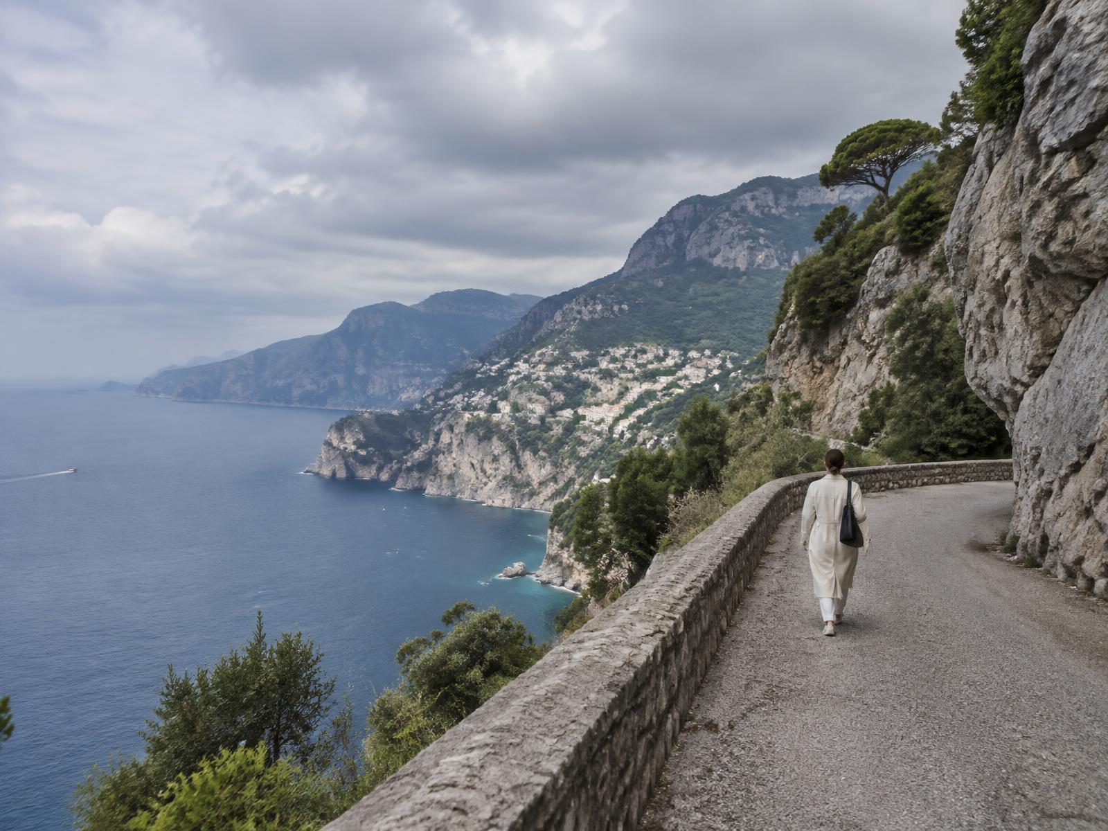 A lone figure walking away along a coastal cliff road above the sea
